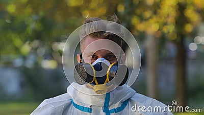 Portrait of man in white protective suit, glasses and respirator looking at camera on city street background. Virologist Stock Photo