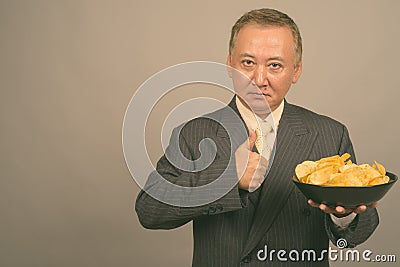 Portrait of mature Asian businessman with bowl of potato chips Stock Photo