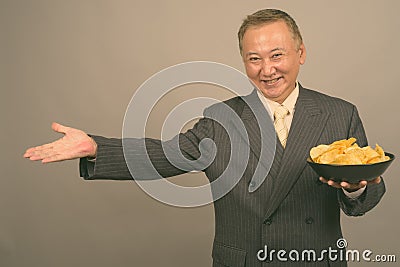 Portrait of mature Asian businessman with bowl of potato chips Stock Photo