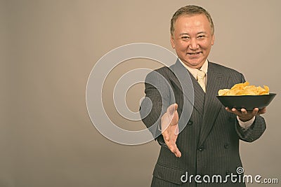 Portrait of mature Asian businessman with bowl of potato chips Stock Photo