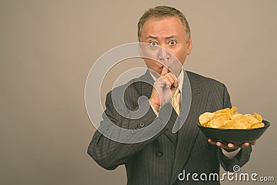 Portrait of mature Asian businessman with bowl of potato chips Stock Photo