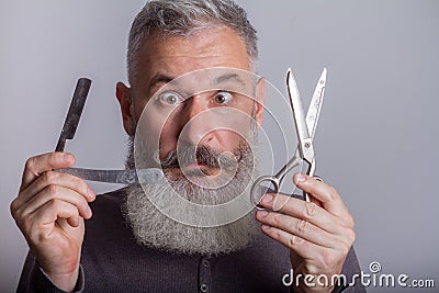 Portrait of mature bearded man with retro razor and scissors, barbershop concept, selective focus Stock Photo