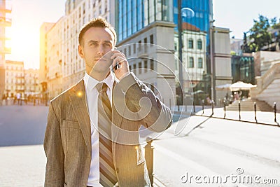 Portrait of mature confident businessman smiling and talking on smartphone while walking on pavement Stock Photo