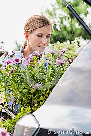 Portrait of mature female gardener putting flowers on car trunk for delivery Stock Photo