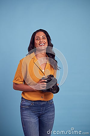Portrait Of Mature Female Photographer With Camera Against Blue Background On Shoot In Studio Stock Photo
