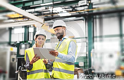 A portrait of an industrial man and woman engineer with tablet in a factory, talking. Stock Photo