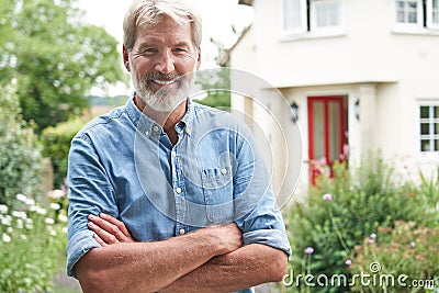 Portrait Of Mature Man Standing In Garden In Front Of Dream Home In Countryside Stock Photo