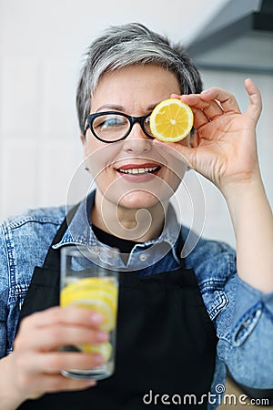 Portrait of a mature smiling woman with a glass of lemon water in the kitchen Stock Photo