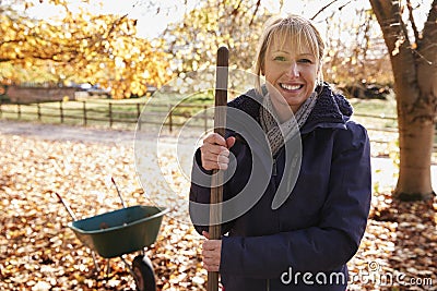 Portrait Of Mature Woman Raking Autumn Leaves In Garden Stock Photo