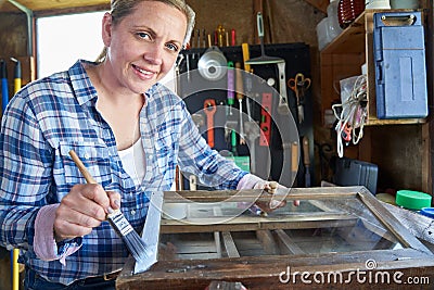 Portrait Of Mature Woman Upcycling Furniture In Workshop At Home Painting Cabinet Stock Photo