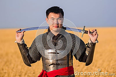 Portrait of a medieval warrior in armor with a weapon in his hands against the background of a wheat field and sky Stock Photo
