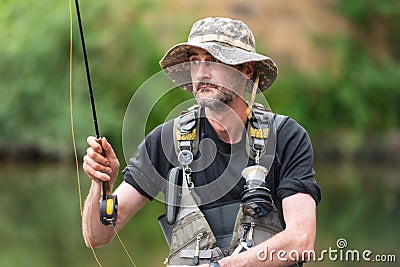 Portrait of mid adult fisherman on river, relaxing and fishing trouts. Stock Photo