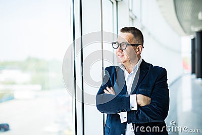 Portrait of a middle aged businessman in front of office window. Man is smiling and has his arms folded. Stock Photo