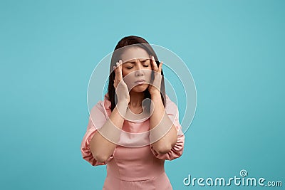 Portrait of middle aged female suffers from migraine, has terrible headache, keeps hand on temples, feels pain and Stock Photo