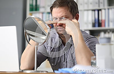 Portrait of middle-aged man sitting opposite small table mirror and squeezing acne problems Stock Photo
