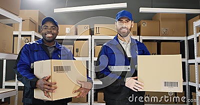 Portrait of mixed-races young male postmen in uniforms and caps holding carton boxes in hands. Stock Photo