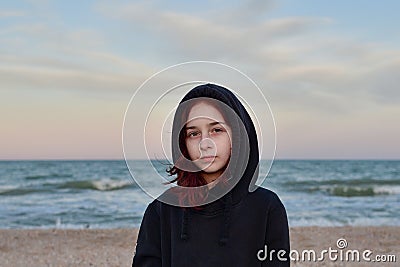 Portrait Of A Model In A Fashionable Jacket At Sunset By the sea. Teenager in a black hoodie and the sea. 9 years old Stock Photo