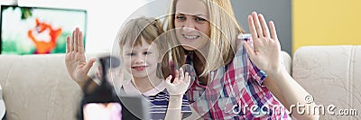 Mother and daughter wave hello on video, videocamera set on tripod Stock Photo