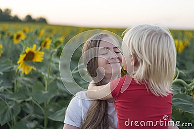 Portrait of mother and little son on field of sunflowers background. Young mother holds her son Stock Photo