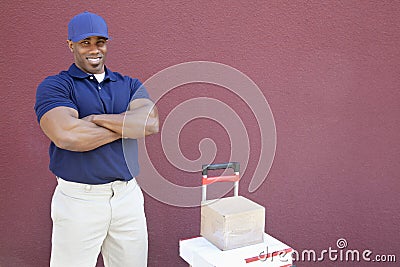 Portrait of a muscular African American man standing with arms crossed and handtruck over colored background Stock Photo