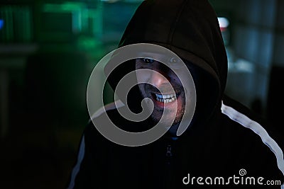 Portrait of mysterious hooded hacker with evil face sitting at desk and breaking into government data servers Stock Photo