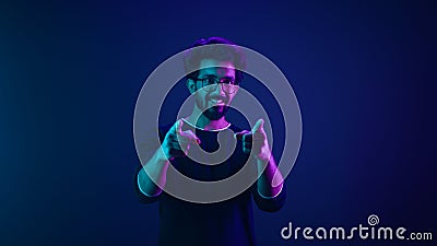 Portrait in neon ultraviolet happy Indian guy Arabian man worker coder hacker computer engineer make gesture hey you Stock Photo
