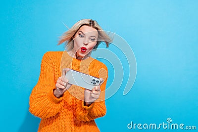 Portrait of overjoyed woman fluttering hair dressed knitwear sweater look at smartphone in hands isolated on blue color Stock Photo