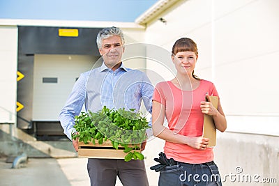 Portrait of owner with crate standing by female botanist against plant nursery Stock Photo
