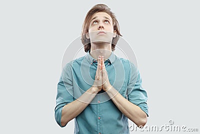 Portrait of palm hands handsome long haired blonde young man in blue casual shirt standing looking up and pray or begging to God Stock Photo