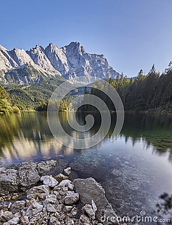 Portrait panorama of the crystal clear water of the Eibsee with the Zugspitze mountain including reflection in the background Stock Photo