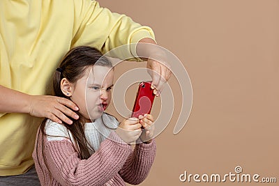 Portrait of parent taking smartphone away from girls hands, beige background. Angry daughter hold tight phone and resist Stock Photo