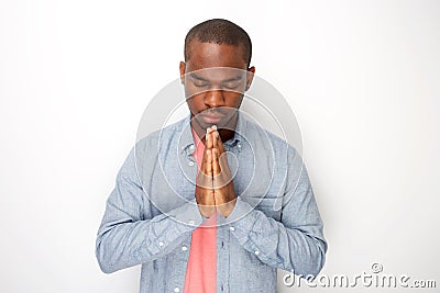 Peaceful young black man praying with hands clasp together by white wall Stock Photo