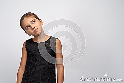 Portrait of pensive pretty girl brunette in a black dress. Beautiful doubtful indecisive child looking up thoughtful Stock Photo