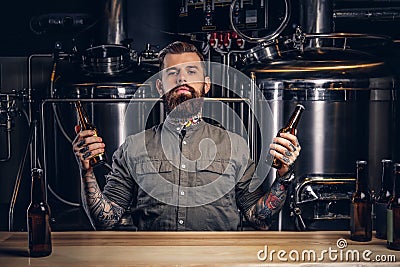 Portrait of a pensive tattooed hipster male with stylish beard and hair hold two bottles with craft beer in the indie Stock Photo