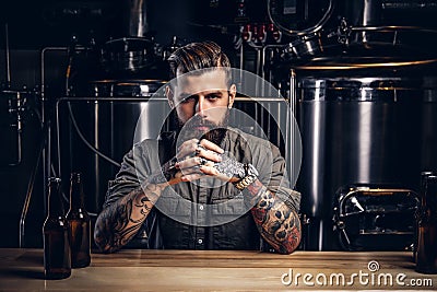 Portrait of a pensive tattooed hipster male with stylish beard and hair in the shirt in indie brewery. Stock Photo