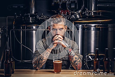 Portrait of a pensive tattooed hipster male with stylish beard and hair in the shirt in indie brewery. Stock Photo