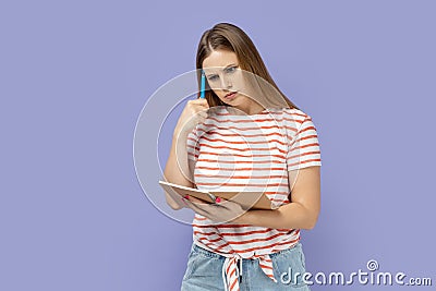 Pensive thoughtful woman writing in paper notebook, thinking about task, keeps pen near temple. Stock Photo