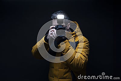 Photographer in a yellow coat taking a photo with flash with a black background Stock Photo