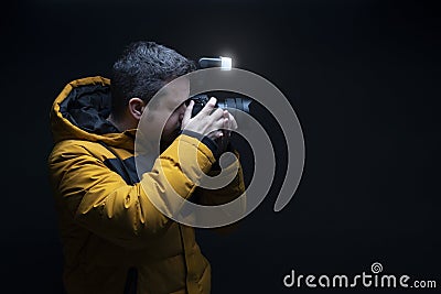 Photographer in a yellow coat taking a photo with flash with a black background Stock Photo