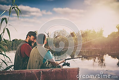 Handsome father and son sitting in boat on lake while enjoying fishing together Stock Photo