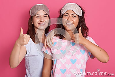 Portrait of pleasant energetic young cute women having pleasant facial expressions, having pajamas party, raising hands, showing Stock Photo
