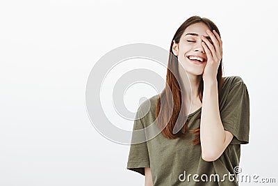 Portrait of pleased confident good-looking urban female in dark-green t-shirt, holding palm on face and smiling broadly Stock Photo