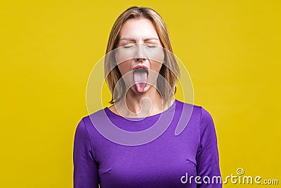 Portrait of positive carefree woman demonstrating tongue. indoor studio shot isolated on yellow background Stock Photo