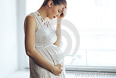 A portrait of pregnant woman has headache staying near window at home Stock Photo