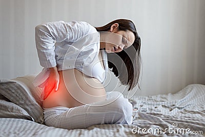 Portrait of a pregnant woman on the side of the bed holding the waist. back pain, pregnancy difficulties Stock Photo