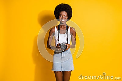 Portrait of pretty cheerful slim wavy-haired girl holding in hands digicam shooting picture isolated over bright yellow Stock Photo