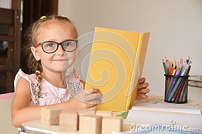 Portrait of pretty female kindergarten student sitting in the classroom while reading textbooks.little girl sitting at a desk and Stock Photo