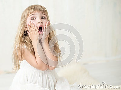 Portrait of pretty little girl in white dress , she is surprised and put her hands on cheeks. Stock Photo