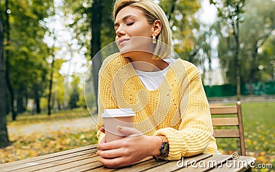 Portrait of pretty young woman drinking coffee at terrace cafetaria in the park. Female in the city street drinking hot cappuccino Stock Photo