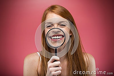 Pretty young woman showing teeth trought magnifying glass over pink background. Stock Photo